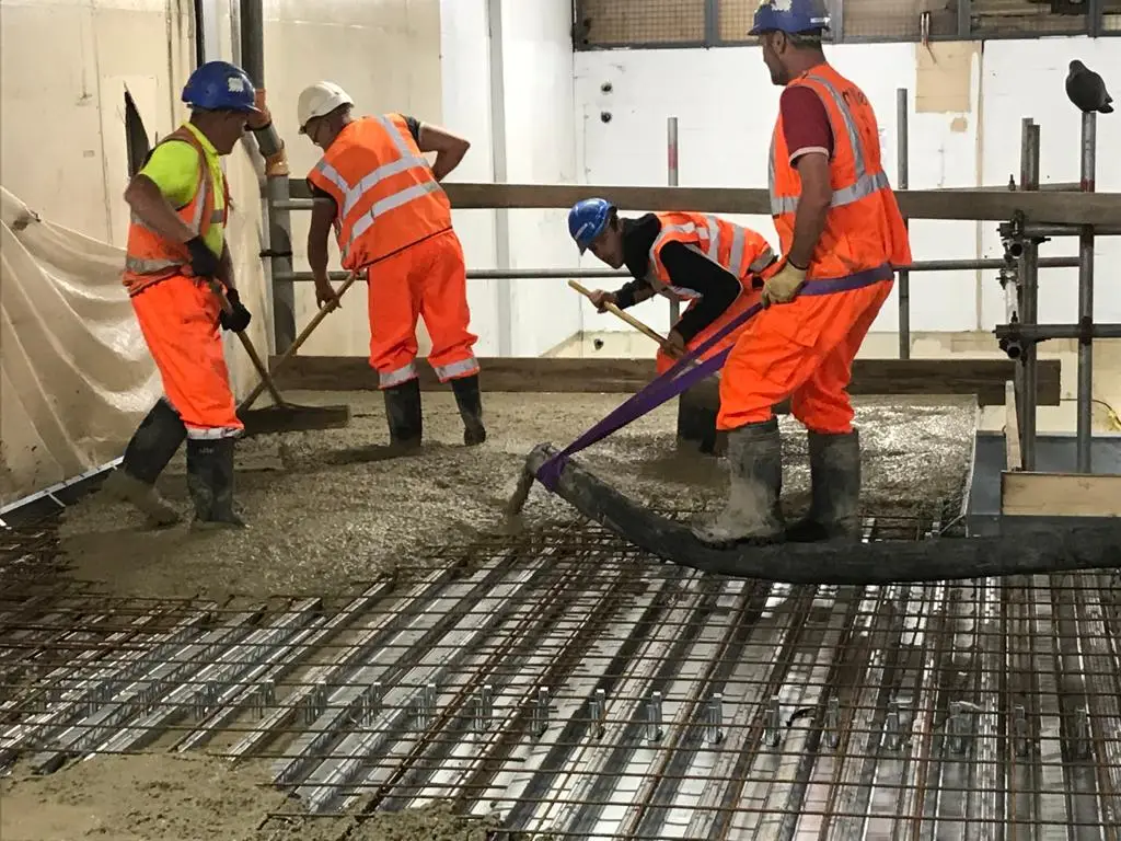 Site team pouring and levelling concrete over metal floor decking and reinforcement mesh