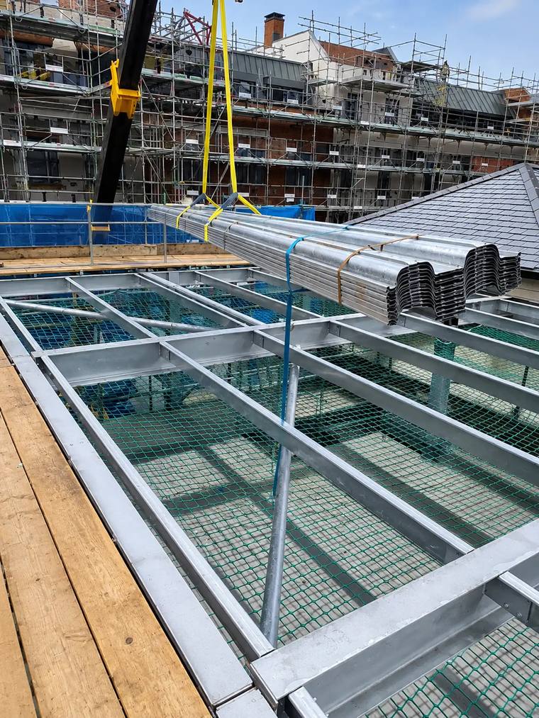 Metal roof decking craned onto steel beams with safety netting below